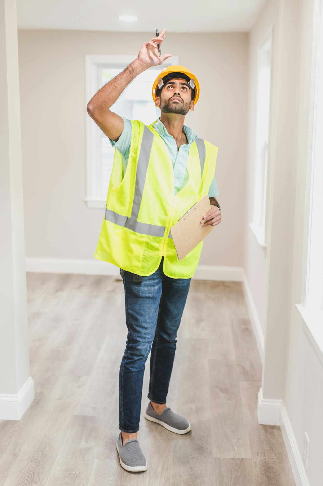 Construction worker in safety vest and hard hat inspecting ceiling indoors.